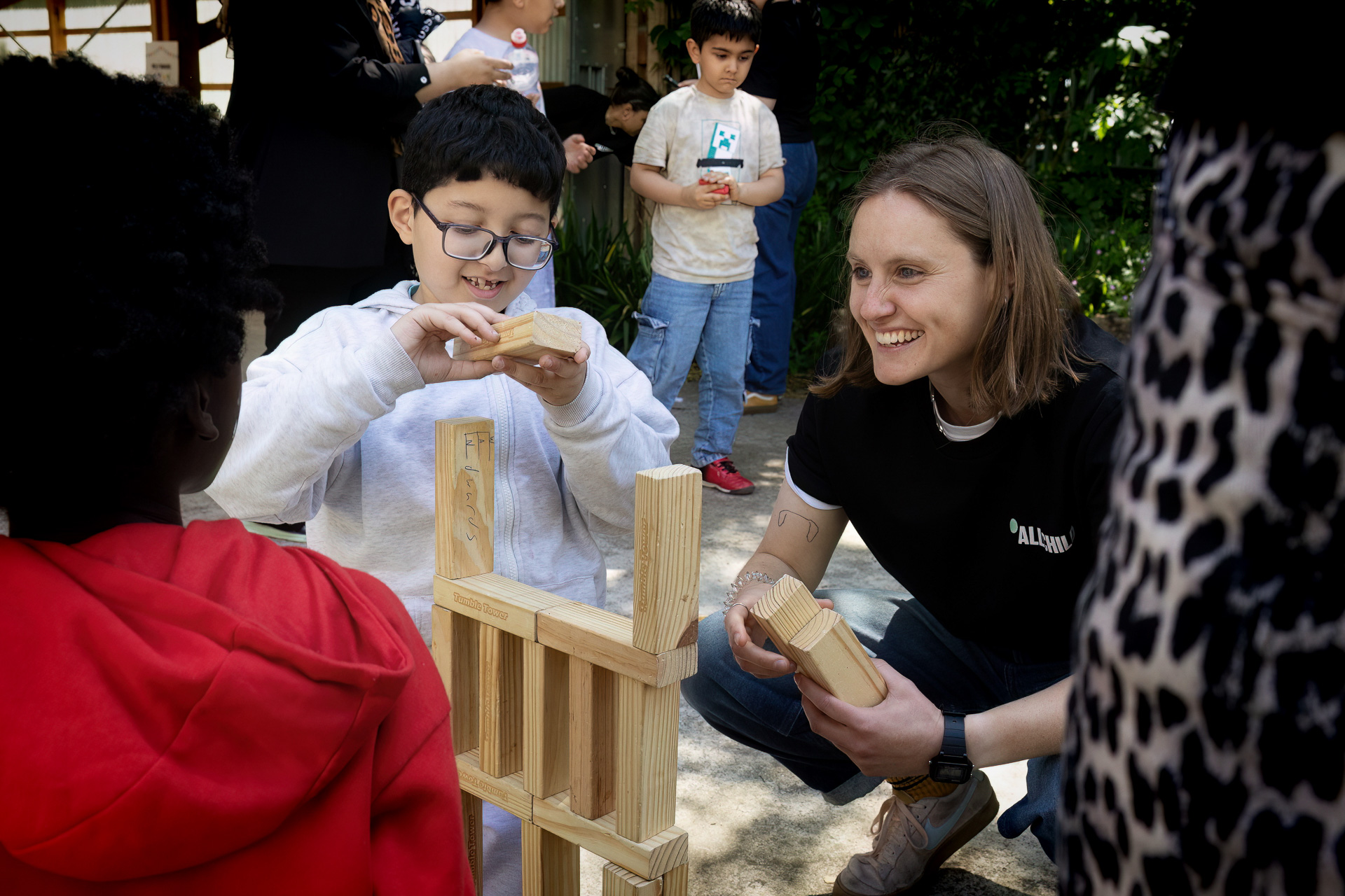 link worker and male primary child playing with wooden blocks outside